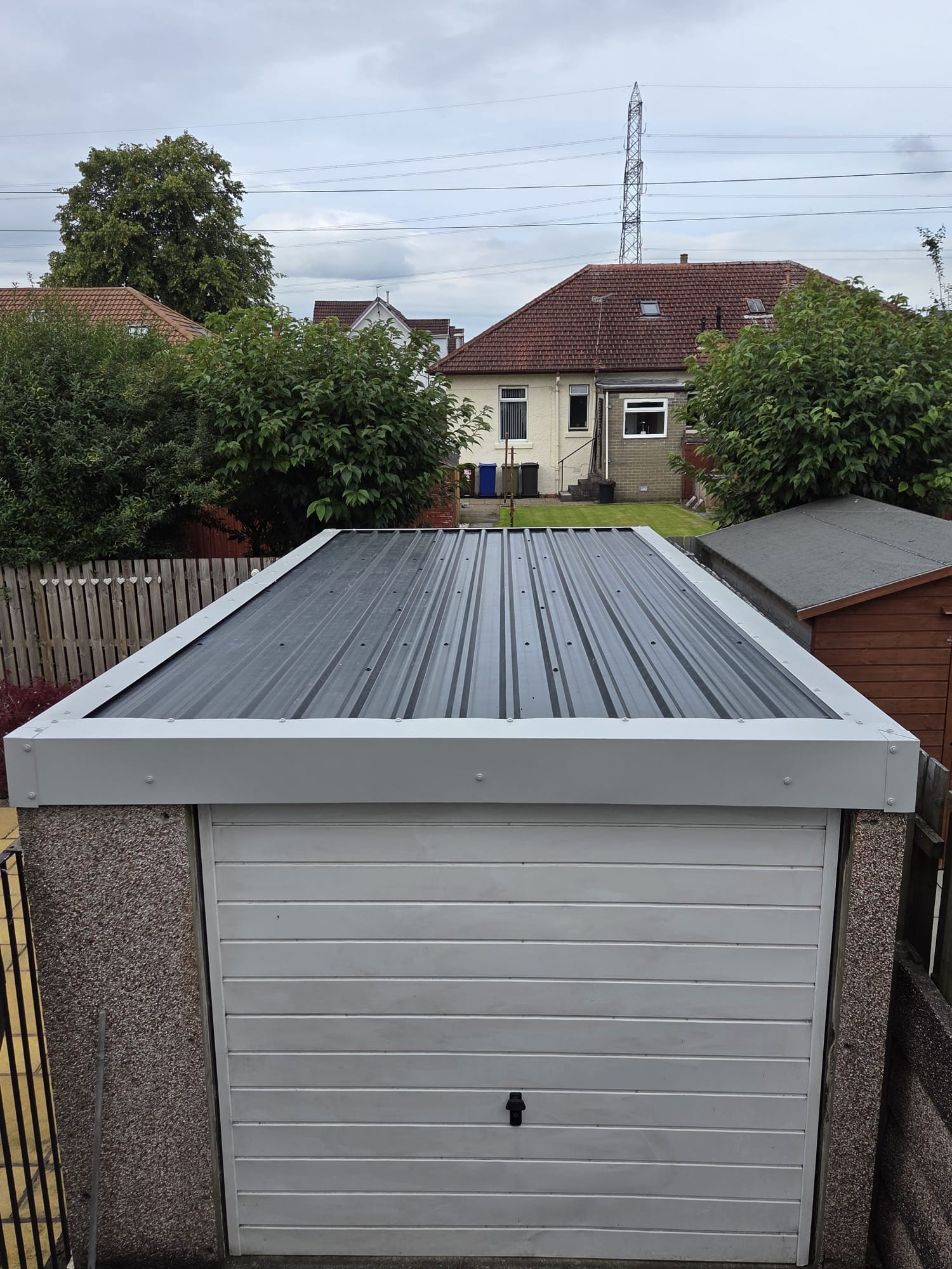 Completed grey profiled garage roof with white perimeter trims and a white garage door