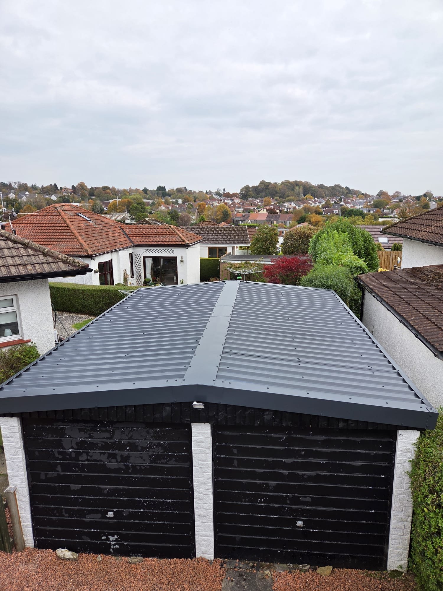 Completed grey metal overcladding on a double garage roof with matching ridge and edge trims