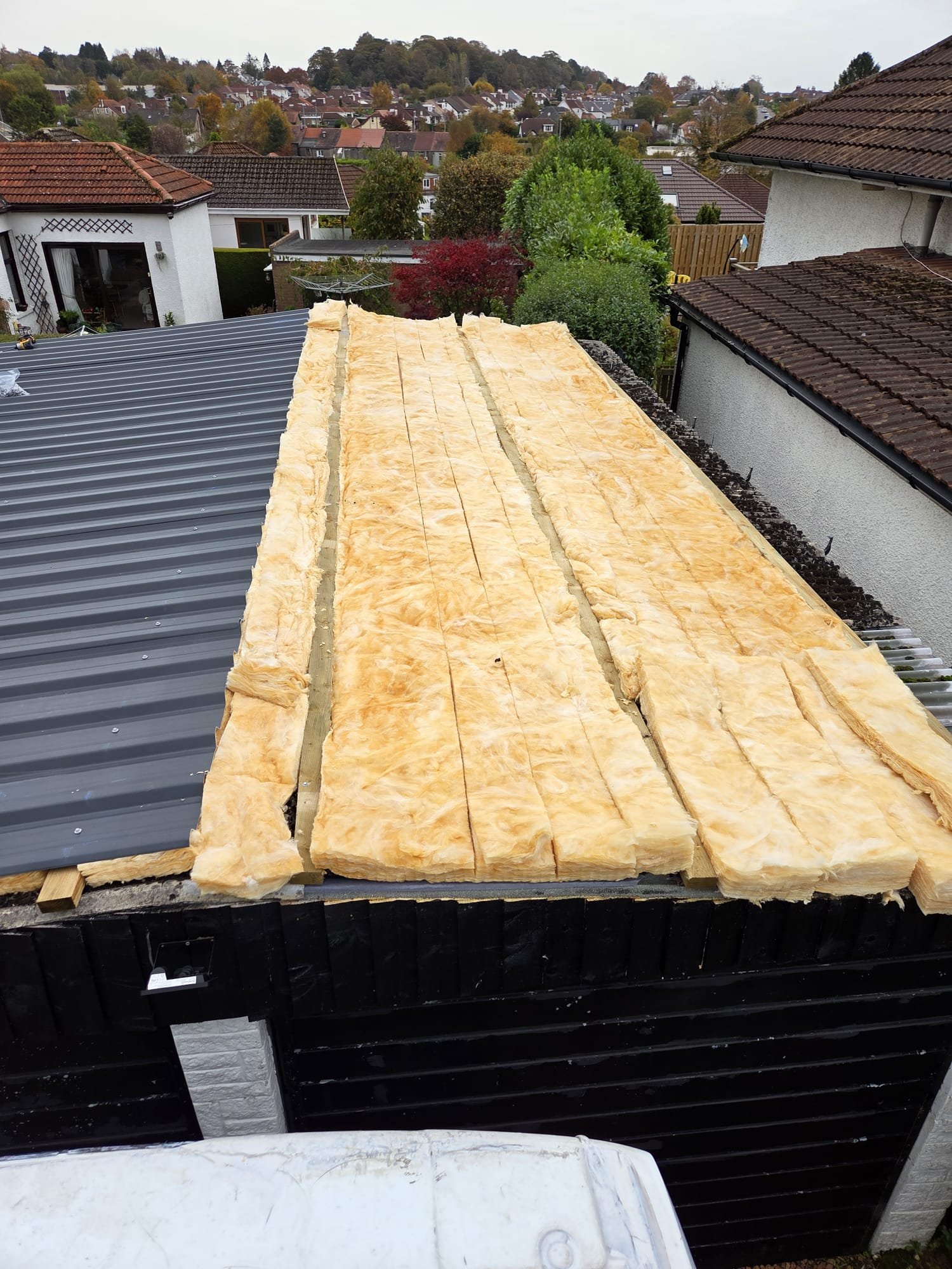 Grey metal roof sheets being fitted over insulation on a double garage